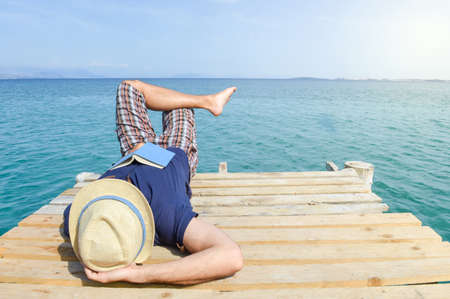 Man lying on the dock with a book. Summer vacation relaxationの写真素材