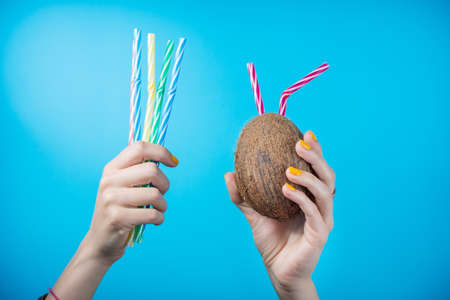 Womans hand holding a coconut and straws against blue backgroundの写真素材