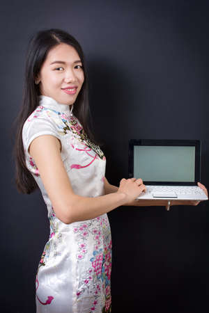 Young asian woman holding a laptop wearing chinese dressの写真素材