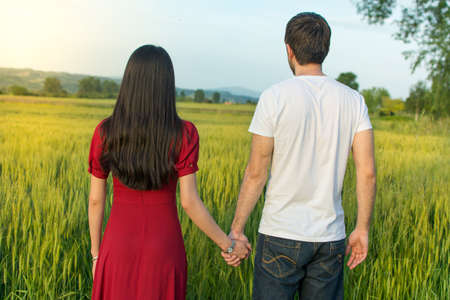 Couple holding hands in a wheat field facing sunset