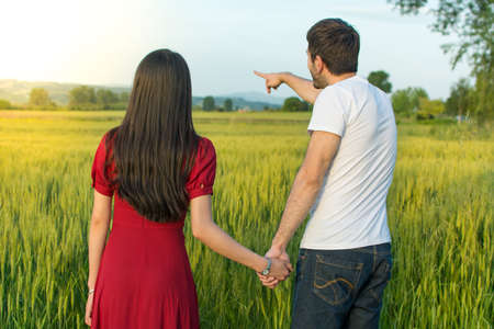 Couple holding hands in a wheat field facing sunset