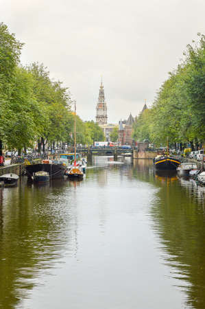AMSTERDAM - SEPTEMBER 17, 2015: View at the famous clock tower of the Zuiderkerk thro Amsterdam canal with some tourist passing during dayのeditorial素材