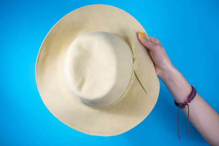 Woman hand holding a hat against blue background