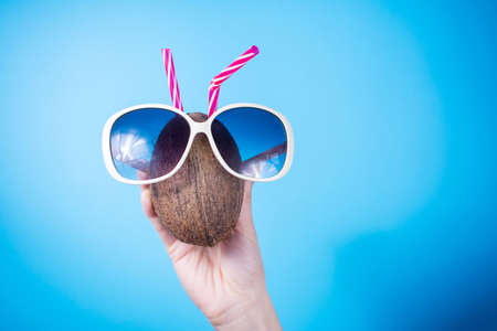 Woman hand holding a coconut and sunglasses against blue backgroundの写真素材