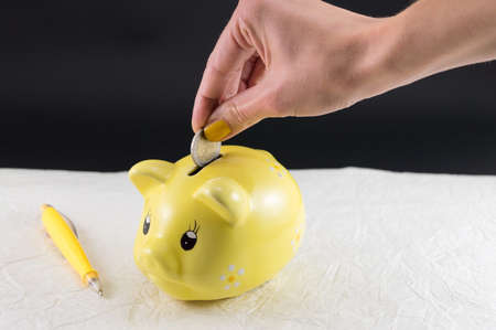 Woman hand inserting a coin into piggy bankの写真素材