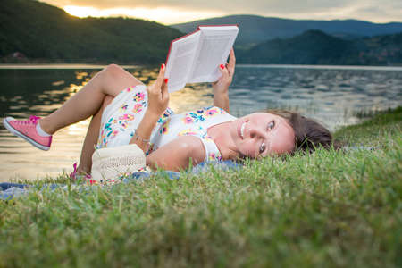 Young woman reading a book by the lake. Solo relaxationの写真素材
