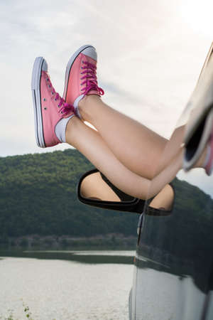 Woman legs out of the car window by the lake
