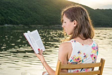 Young woman reading a book by the lakeの写真素材