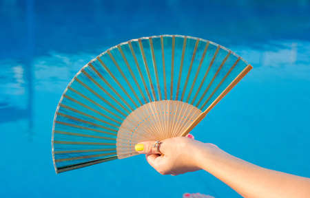 Hand fan in girls hand by the swimming poolの写真素材