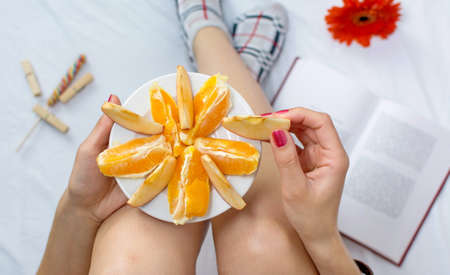 Woman eating fresh orange fruit in bed