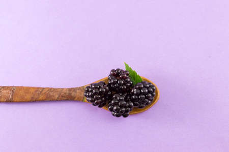 blackberries in a wooden spoon on a purple backgroundの写真素材