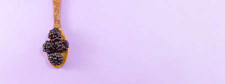 blackberries in a wooden spoon on a purple backgroundの写真素材