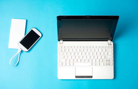 White laptop and smart phone charging on power bank on blueの写真素材