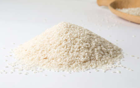 Pile of rice and big wooden spoon on white backgroundの写真素材