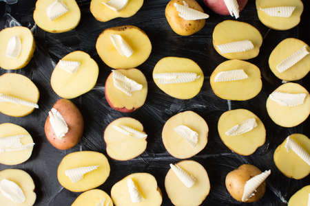 Raw potato with butter on black baking plate