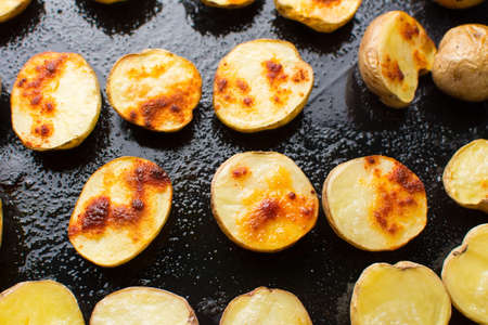 Roasted potato slices on a black baking plateの写真素材