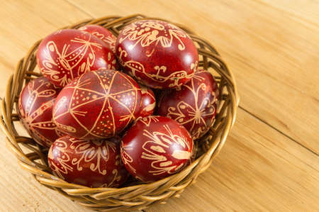 Wax decorated red Easter eggs in a wicker bowlの写真素材