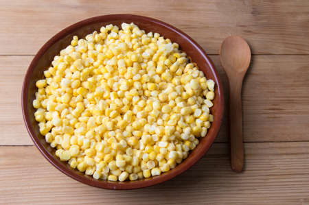 Frozen sweet corn in a bowl with a wooden spoonの写真素材