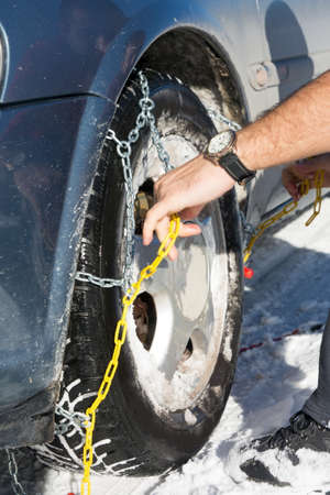 Man mounting snow chains on car wheels