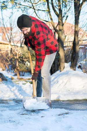 bearded man shoveling snow in a checked shirtの写真素材