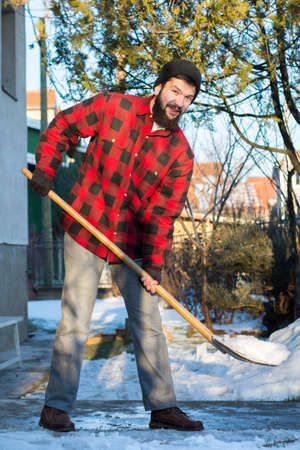 bearded man shoveling snow in a checked shirtの写真素材