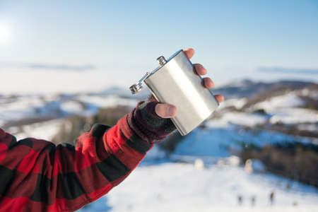 Male hand holding hip flask on a snowy mountain topの写真素材