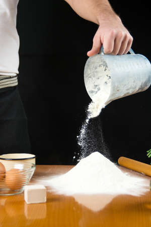 Man pouring flour from the measure bowl on the tableの写真素材
