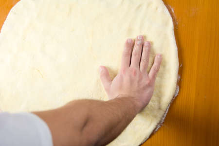 Male baker spreading the dough for making pizzaの写真素材