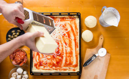 Man grating cheese on a pizza base. Making pizza