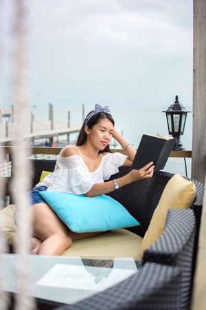Girl reading a book on the balcony with seaside viewの写真素材