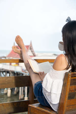 Girl reading a book on the balcony with seaside viewの写真素材