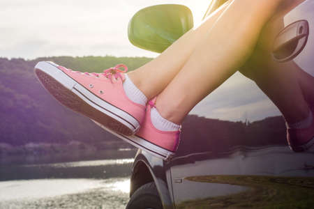 Woman legs out of the car window by the lake at sunsetの写真素材