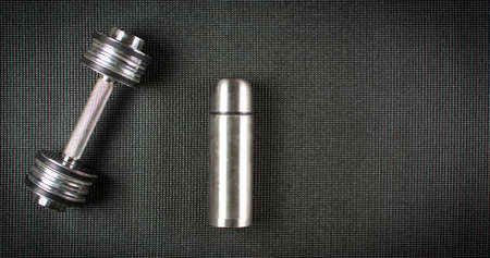 Metal dumbbell and water bottle on black yoga matの写真素材