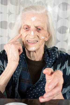 Cheerful grandma applying face cream at homeの写真素材