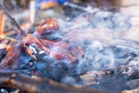 Sausages roasting on burning embers outdoors on a picnic