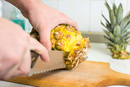 Hands cutting  fresh pineapple on a wooden board
