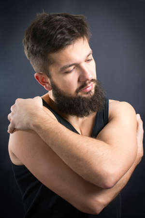 Lonely bearded man hugging himself against black backgroundの写真素材