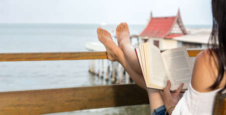 Girl reading a book on the balcony with seaside viewの写真素材