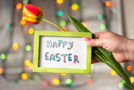 Hand holding Happy Easter card and a red tulipの写真素材