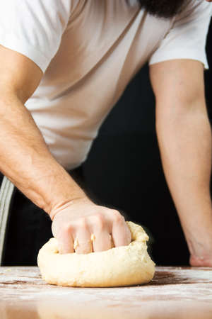 Male baker punching dough from the kitchen table