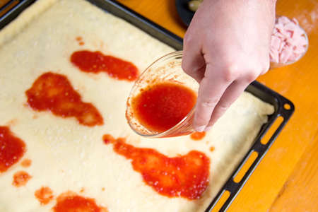 Man putting tomato sauce on raw pizza baseの写真素材