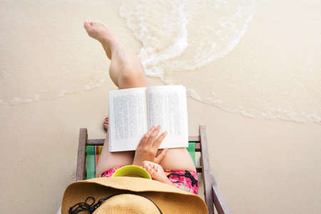 Girl reading a book in sunbed at the beachの写真素材