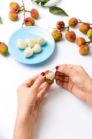 Female hands peeling lychee fruit on whiteの写真素材