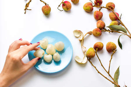 Woman taking lychee tropical fruit from a blue plateの写真素材