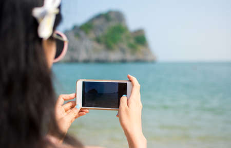 Girl taking a picture with smart phone on the beachの写真素材