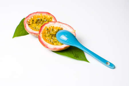 Halved passion fruit with a blue spoon isolated on whiteの写真素材