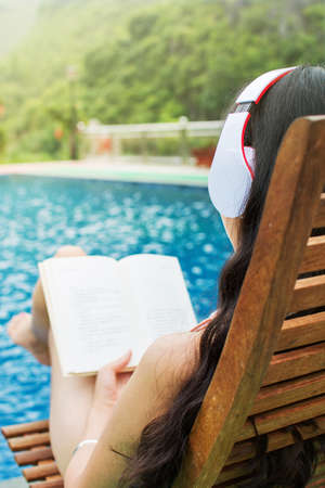Girl reading a book by the swimming poolの写真素材