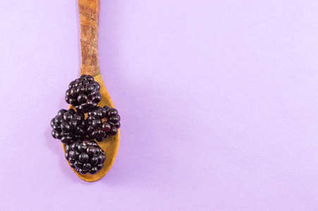 blackberries in a wooden spoon on a purple backgroundの写真素材