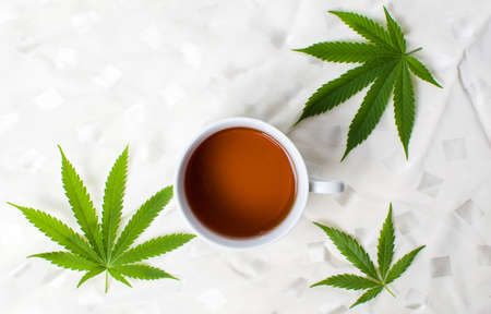 Cannabis tea and marijuana leaves on white fabric top viewの写真素材