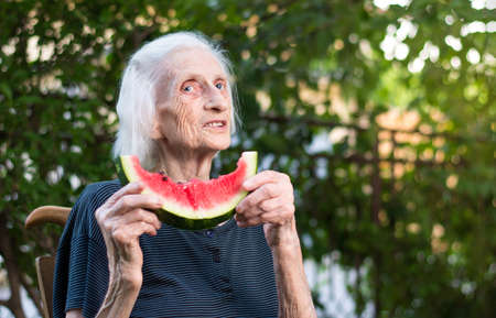 Senior woman holding watermelon slice in the backyardの写真素材